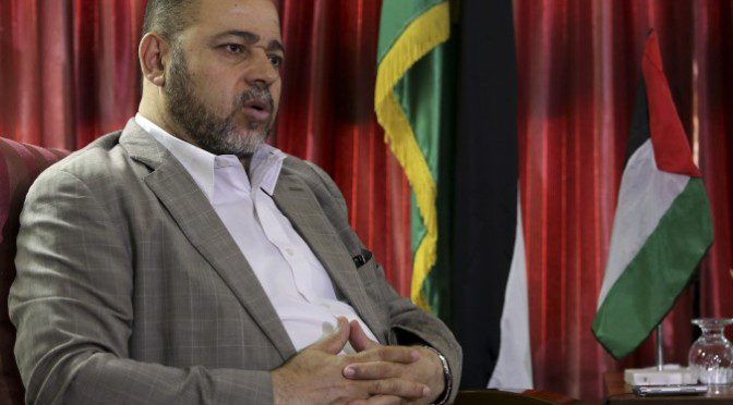 Seated man with hands clasped, flags behind